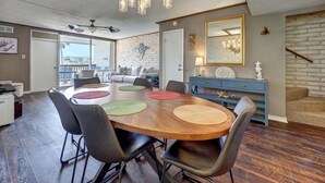 A modern dining area with a wooden table, black chairs, and a hanging light fixture. - Charming Coral Cay #207: 2BR condo with pool view in Port Aransas. (Port Aransas)