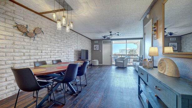 A modern dining area with a brick wall, wooden flooring, and a large table with chairs. - Charming Coral Cay #207: 2BR condo with pool view in Port Aransas. (Port Aransas)