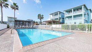Piscina com cerca branca, rodeada por edifícios com varandas e palmeiras.