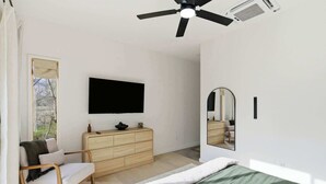A bedroom with a bed, a wooden dresser, a TV, a ceiling fan, and a window. - Overlook at Black Apple | On NWA Trail | Downtown (Bentonville)