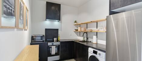 Una cocina compacta equipada con microondas, estufa, horno, lavadora y refrigerador de acero inoxidable.