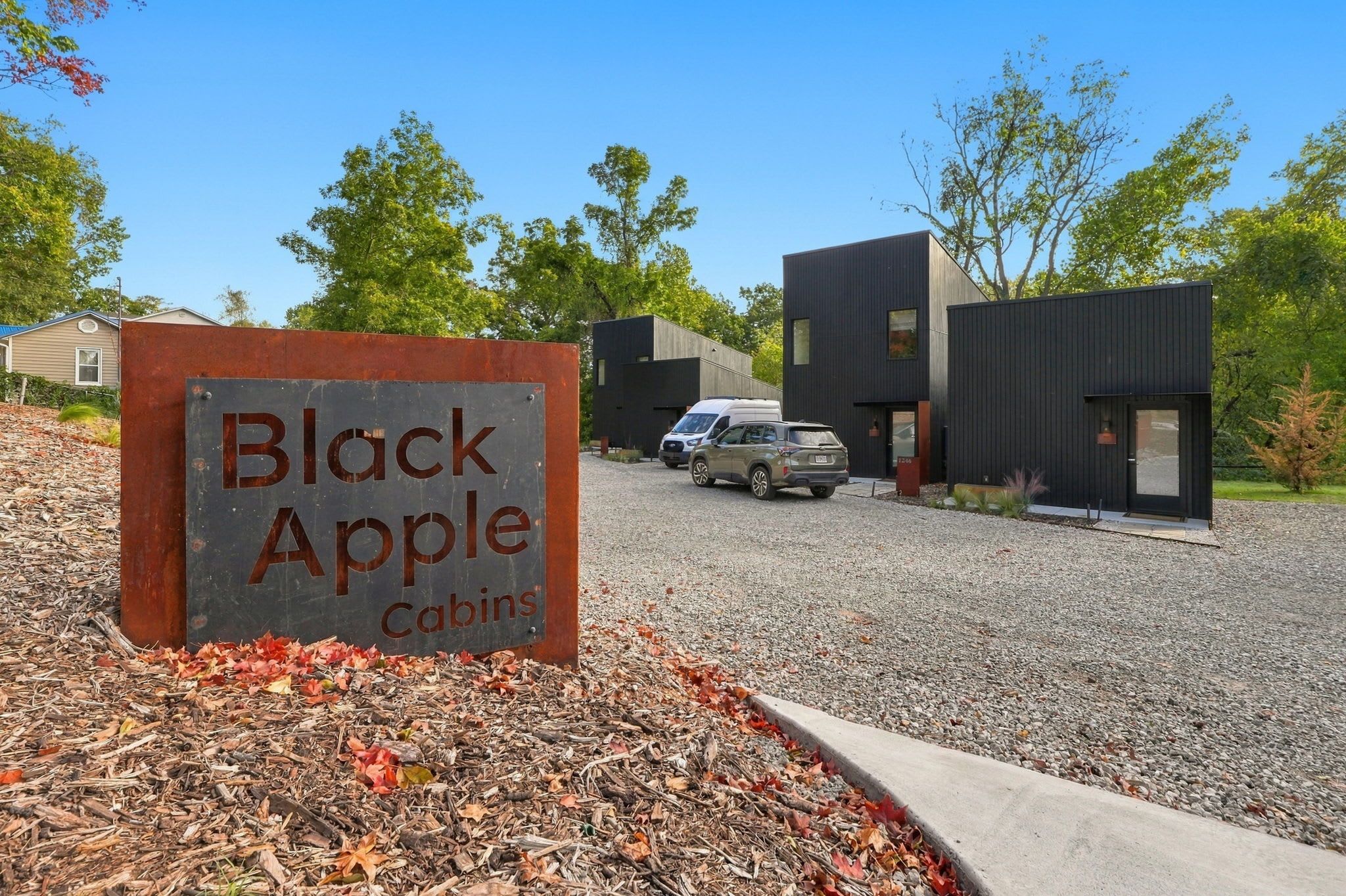 Naamplaatje voor Black Apple Cabins, met een grindpad en moderne cabins op de achtergrond.
