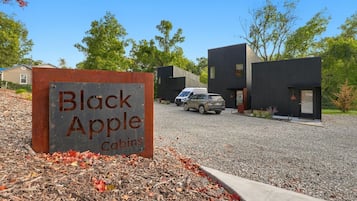 Naamplaatje voor Black Apple Cabins, met een grindpad en moderne cabins op de achtergrond.