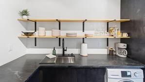 A modern kitchen with a built-in washing machine, a sink, and shelves with dishes and glasses. - Overlook at Black Apple | On NWA Trail | Downtown (Bentonville)
