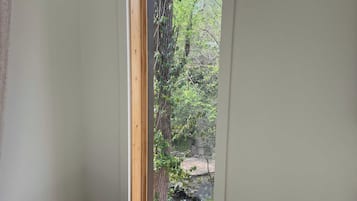 Een kamer met een raam dat uitkijkt op een natuurlandschap, met bomen en een beekje.
