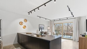 Eine moderne Küche mit Kochinsel, Pendelleuchten und Blick auf eine Terrasse.
