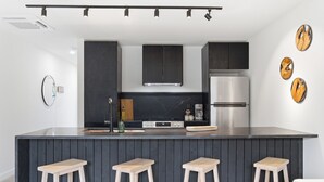 Eine moderne Küche mit dunklen Schränken, einer zentralen Kochinsel mit Hockern, einem Edelstahlkühlschrank und einem wandmontierten Backofen.