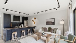 Eine moderne Küche mit Barhocker, einem Essbereich mit Holztisch, einem Sofa und einer Lampe.