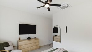 A bedroom with a bed, a dresser, a chair, a ceiling fan, a mounted TV, and a mirror. - Vista at Black Apple | On NWA Trail | Downtown (Bentonville)