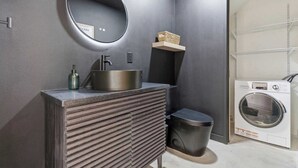 Ein Badezimmer mit Waschbecken, Spiegel, Ablagefläche, Mülleimer und einer Waschmaschine.