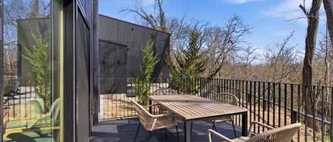 A deck with a table and chairs, a glass door, and a view of trees and sky.