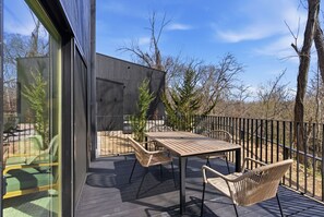 A deck with a table and chairs, a glass door, and a view of trees and sky. - Trailhead at Black Apple | On NWA Trail | Downtown (Bentonville)