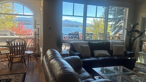 Un salon avec un canapé en cuir, une table basse en verre et une vue sur un lac et des montagnes, grâce à de grandes fenêtres.