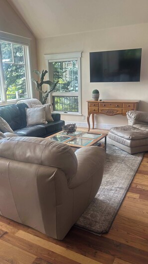 Una sala de estar con un sofá de cuero, una mesa de centro de vidrio, un aparador de madera y un ventanal con vista a árboles.
