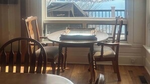 A dining area with a large arched window overlooking a lake and mountains, wooden furniture, and a clock on the wall. - Lakefront Retreat w/ Private Dock & Beach Access (McCall)