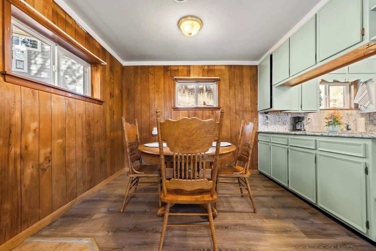 A wooden-paneled room with a dining table and chairs, a window, and green cabinets.