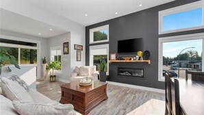 A modern living room with a fireplace, large windows, and a flat-screen TV. - Westcoast Kaatza All Day Sun (Lake Cowichan)