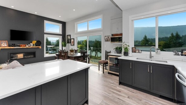 A modern kitchen with a large island, dark cabinetry, and a view of a lake and mountains. - Westcoast Kaatza All Day Sun (Lake Cowichan)