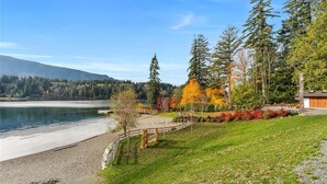 A lakeside property with a wooden deck, a stone pathway, and a view of the lake and forest. - Westcoast Kaatza All Day Sun (Lake Cowichan)