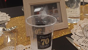 Een tafel met een glas, een lijst met een foto en een plastic beker met een '70 jaar'-etiket.