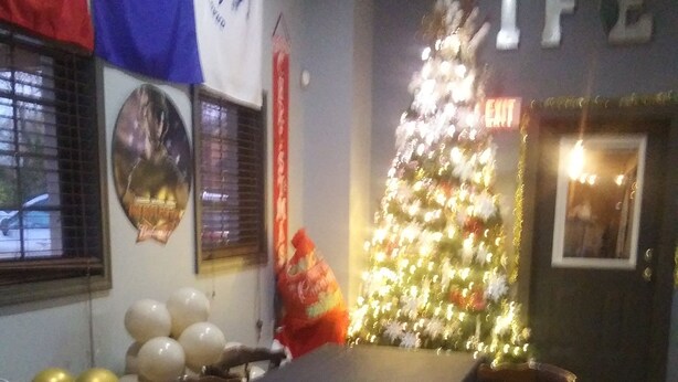 Een eethoek met een lange tafel, stoelen, een kerstboom en vlaggen aan de muur.