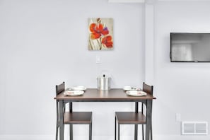 A dining area with a table, chairs, a painting, a TV, and a radiator. - Private 2BR Suite Near Ambassador Bridge (Windsor)
