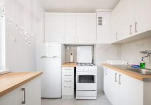 Een kleine keuken met witte kastjes, een inbouwoven en een houten aanrecht.