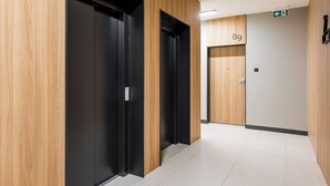 A hallway with wooden paneling and black elevator doors, a white tiled floor, and a door marked with the number 89. - Wola Karolkowa Superior Apartment (Warszawa)