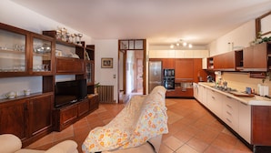 Una sala de estar con sofá, televisión, armarios de madera y un área de cocina con refrigerador y estufa.
