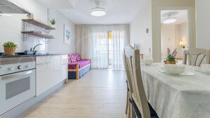 Een moderne keuken met een inbouwoven, een eethoek met een tafel en stoelen, en een zithoek met een bank en een raam.