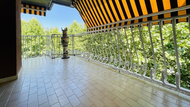 Uma varanda com chão de azulejos, um vaso decorativo e um toldo riscado.