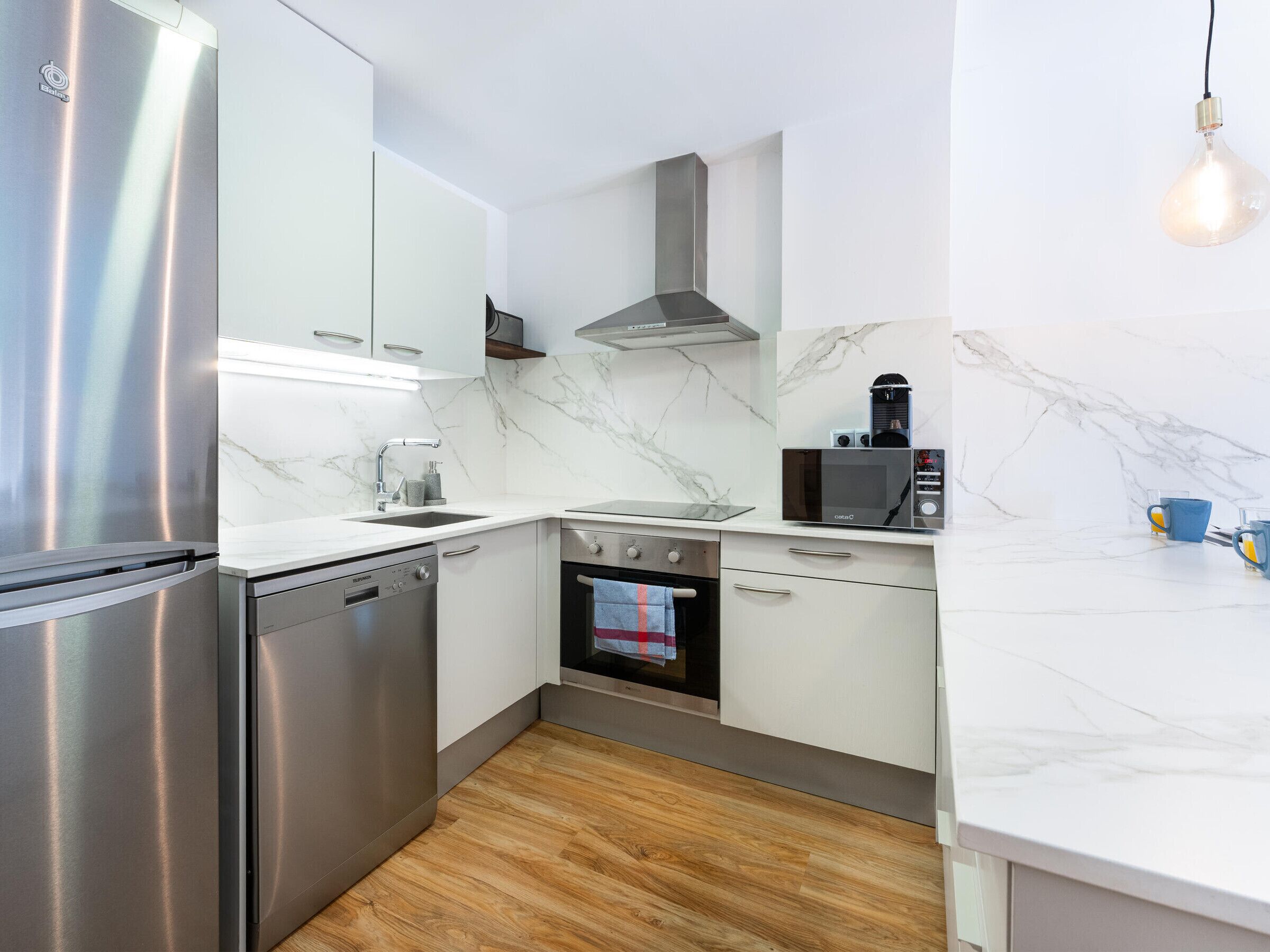 Una cocina moderna con electrodomésticos de acero inoxidable, salpicadero de mármol y piso de madera.