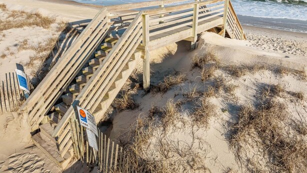 Une promenade en bois mène à une plage, et un panneau indique que l’accès à l’eau est libre.