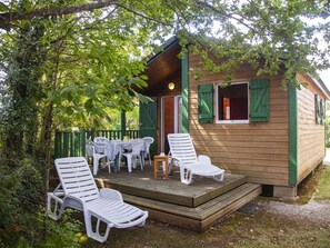 A wooden cabin with a porch, white plastic chairs, and a table. - Chalet with terrace - 4 guests (Naucelle)