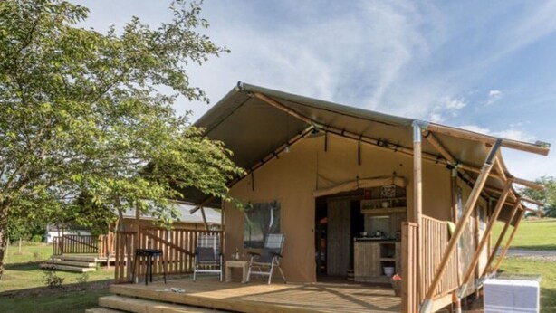 A wooden deck with a covered seating area, a small outdoor kitchen, and a view of a grassy area. - Chalet with terrace - 4 guests (Naucelle)