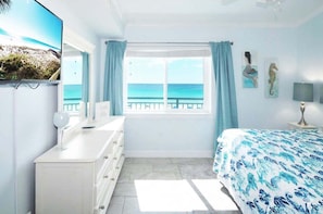 A bedroom with a bed, a dresser, a window with curtains, and artwork on the walls. - Aqua Villa 404: New - Pet Friendly Ocean View, Pool, Parking, & Free Beach Service (Fort Walton Beach)