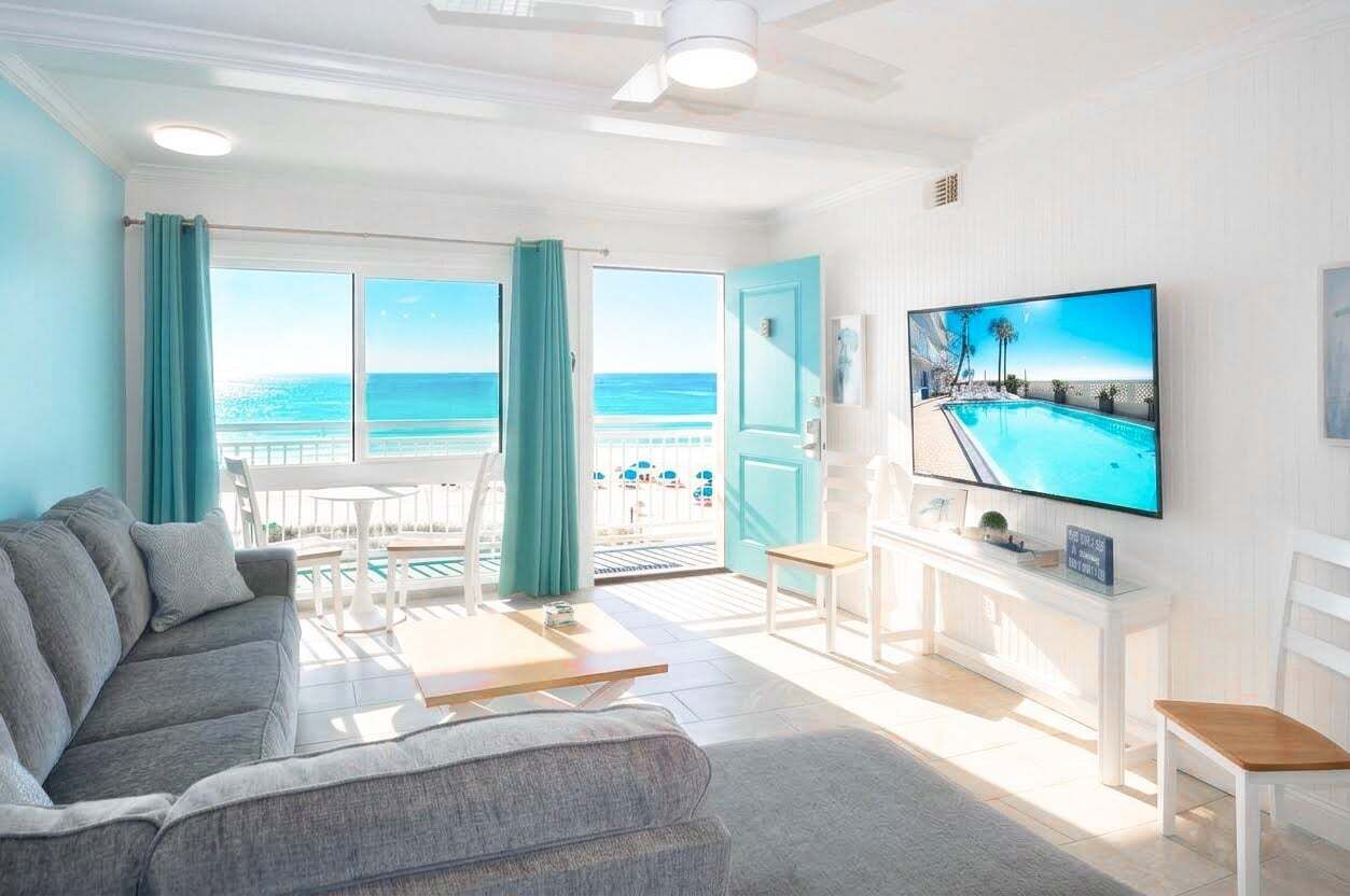 A living room with a sofa, a TV, a pool view, and a balcony with curtains.