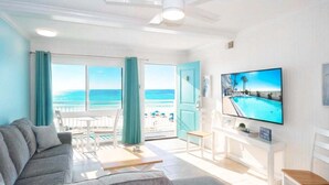 Un soggiorno con divano, televisione, vista sulla piscina e balcone con tende.