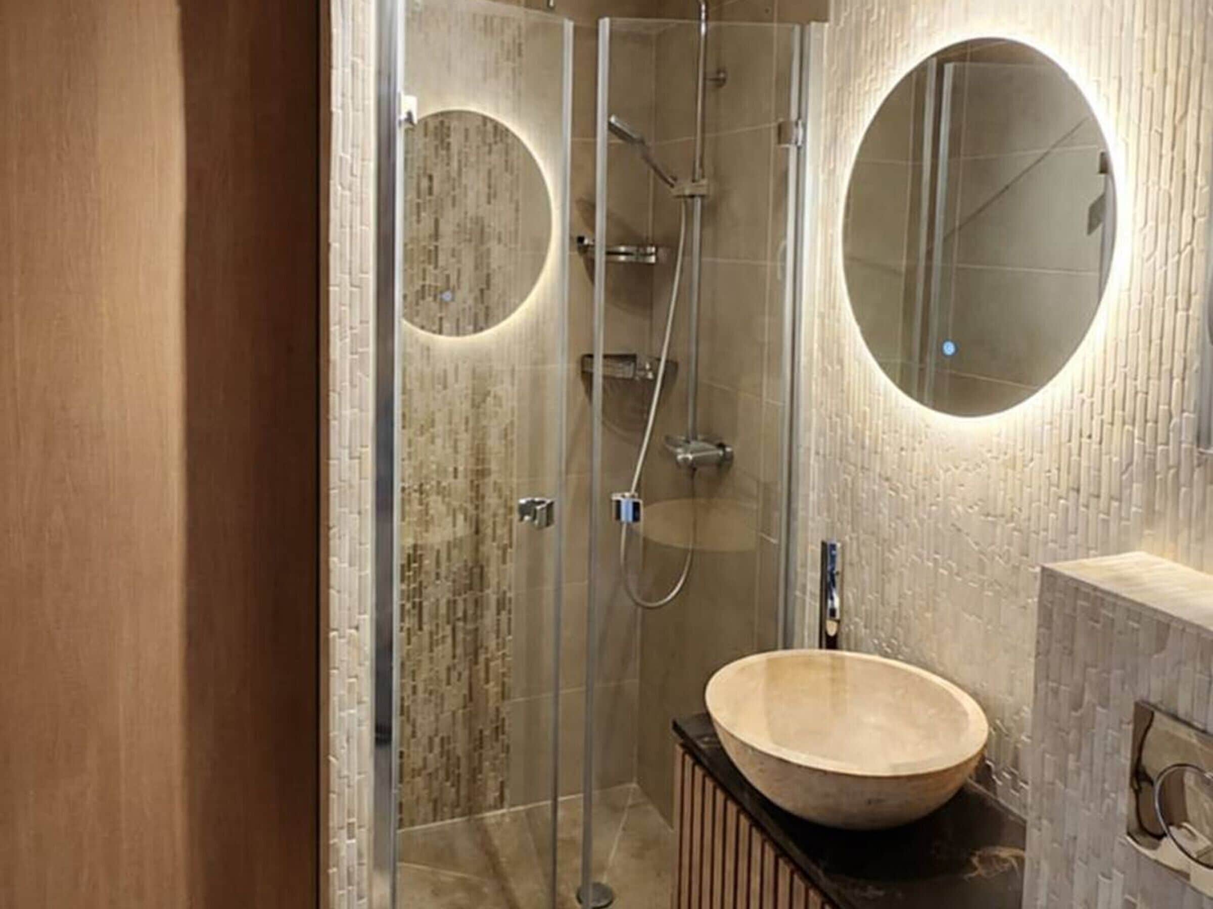 Een moderne badkamer met een douchecabine van glas, een ronde spiegel en een houten wastafel.