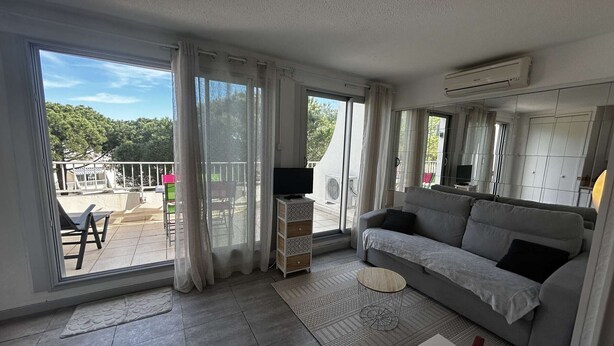 A modern living room with a grey sofa, a small round table, and a TV stand. - Studio cabin with AC and garden view - 4 guests (Port Camargue)