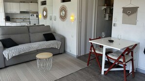 A compact living space with a sofa, dining table, and chairs, a kitchen area, and decorative wall sconces. - Studio cabin with AC and garden view - 4 guests (Port Camargue)