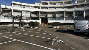 A multi-story building with a parking lot in front, featuring a white van and several potted plants. - Studio cabin with AC and garden view - 4 guests (Port Camargue)