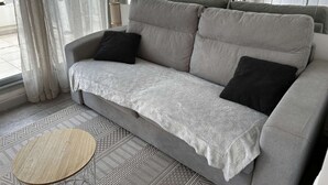A grey sofa with black cushions, a white throw blanket, and a round wooden table. - Studio cabin with AC and garden view - 4 guests (Port Camargue)