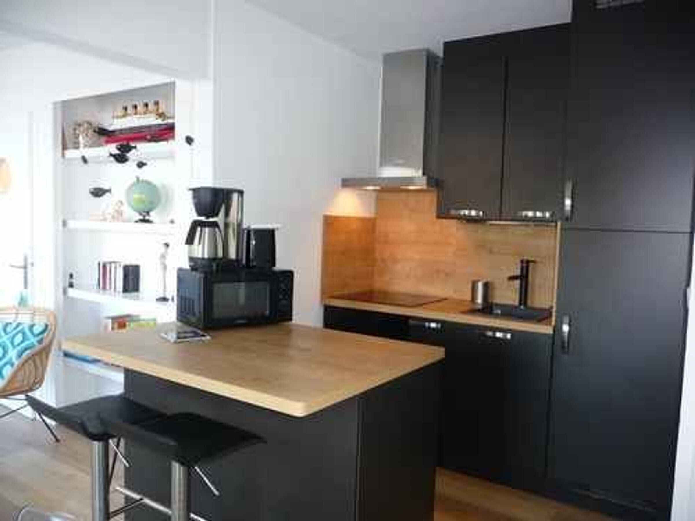 A modern kitchen with a central island, dark cabinetry, and a coffee maker.