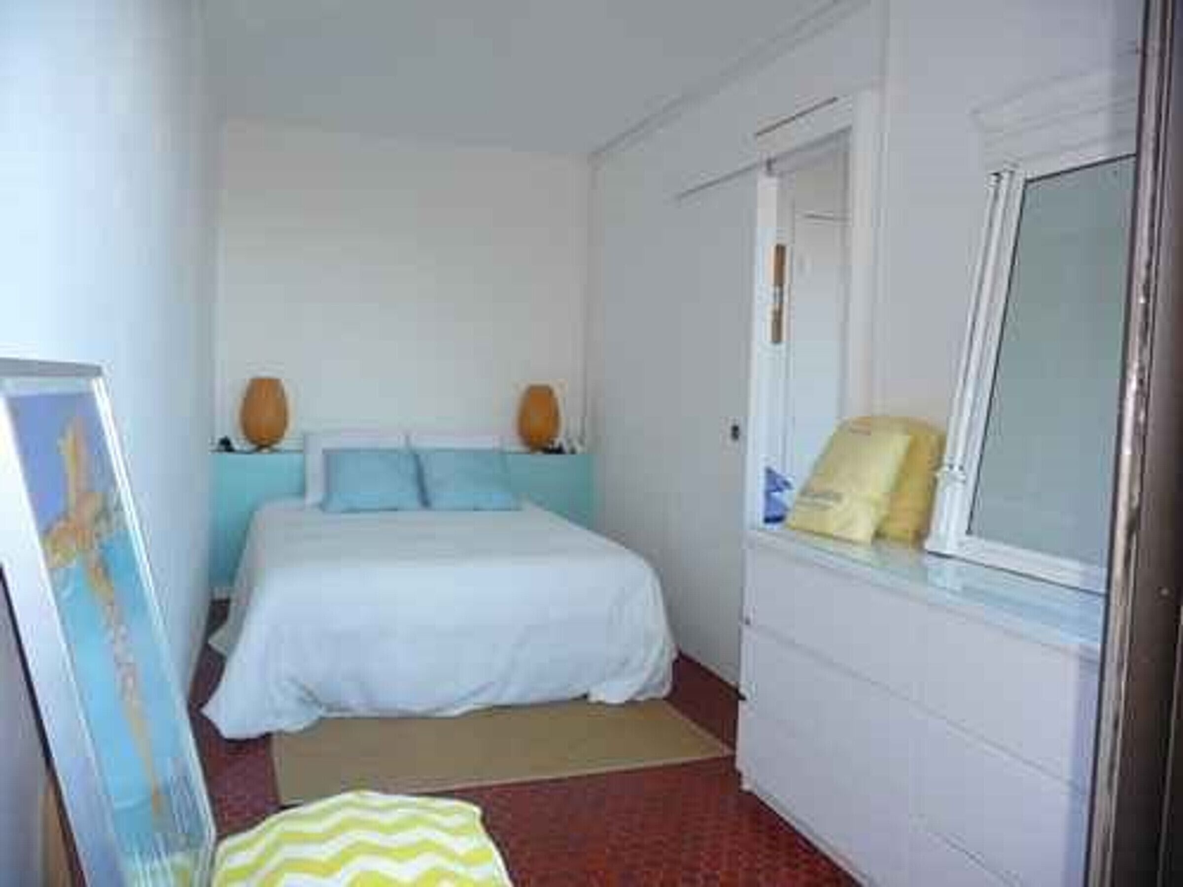 Ein Schlafzimmer mit einem Bett, einem Fenster, einem Spiegel und einem Bild an der Wand.
