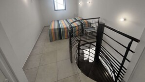 Ein Zimmer mit Etagenbett, Fenster, Treppe und Deckenventilator.