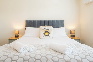 A neatly made bed with a honeycomb-patterned bedspread, two bedside lamps, and a pillow with a bee design.