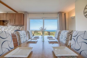 Un comedor con una mesa larga, sillas de estampado geométrico, un jarrón con flores y vistas al exterior.