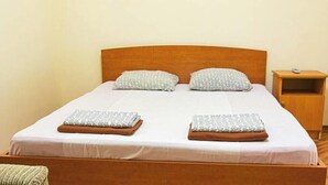 Een enkel bed met houten hoofdbord, twee kussens, een nachtkastje en een klein nachtkastje.