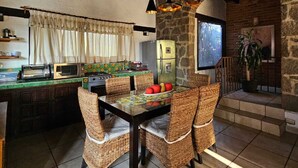 A rustic kitchen with a stone wall, wooden beams, and a dining area with wicker chairs. - Casa con jacuzzi y vista en Valle de Bravo (Valle de Bravo)